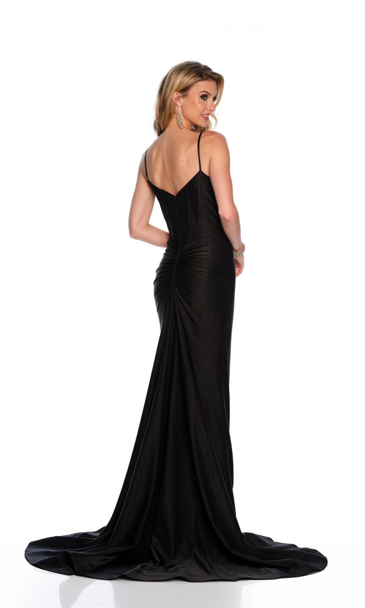 A woman wearing the Long Formal Dress 11553 by Dave and Johnny stands facing away, looking over her shoulder. The black fitted gown with spaghetti straps hugs her silhouette, showcasing timeless elegance.